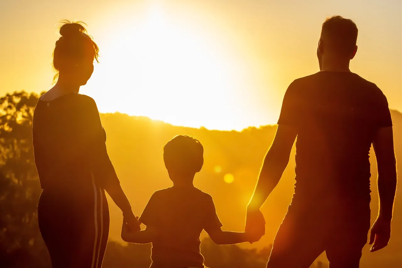 A man and woman holding hands with a boy gaze into the sunset