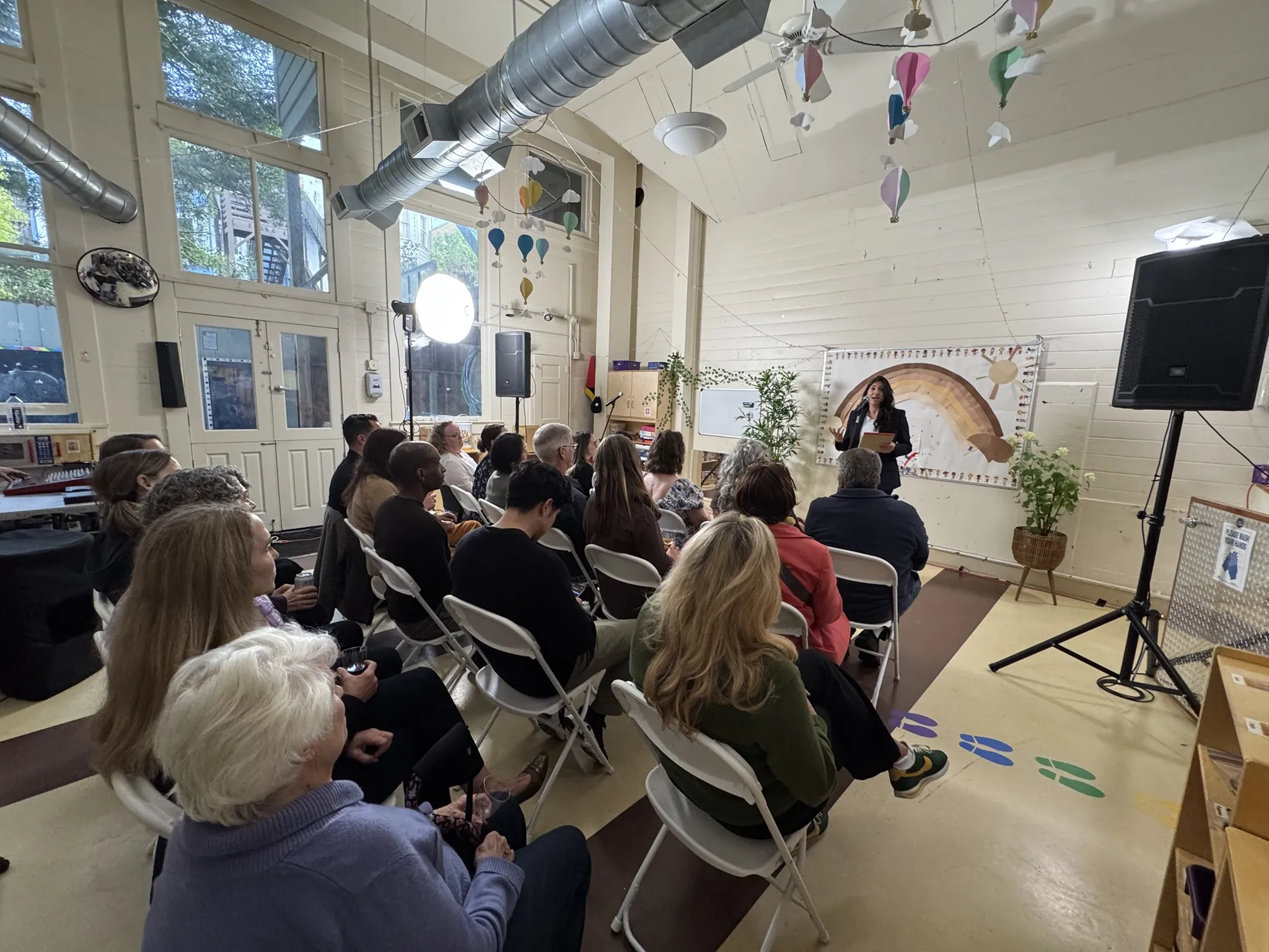 20 audience members in chairs facing towards Dr Pegah Faed who is speaking into a microphone in Safe & Sound's Therapeutic Playroom