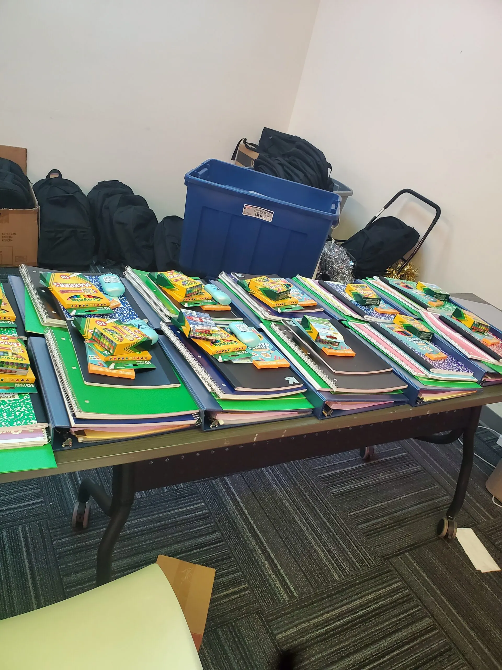 A table laid out with piles of notebooks, folders and crayons